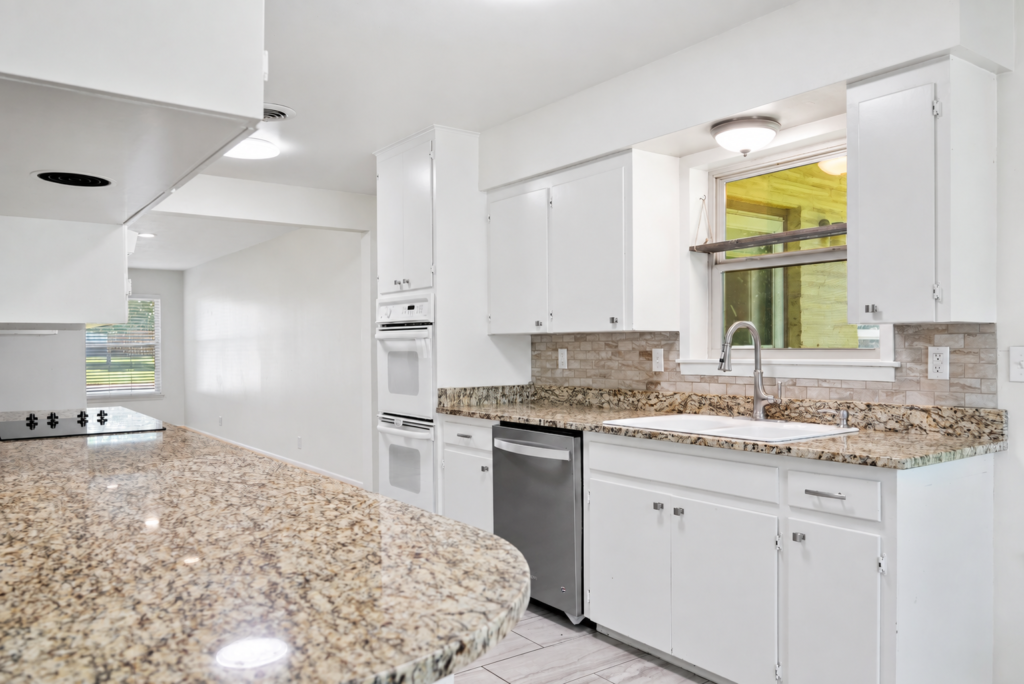 Kitchen with granite island, double wall ovens and white cabinetry
