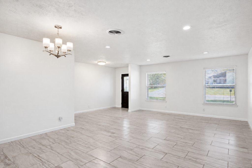 Freshly painted white living and dining area with chandelier and wood-look tile floors
