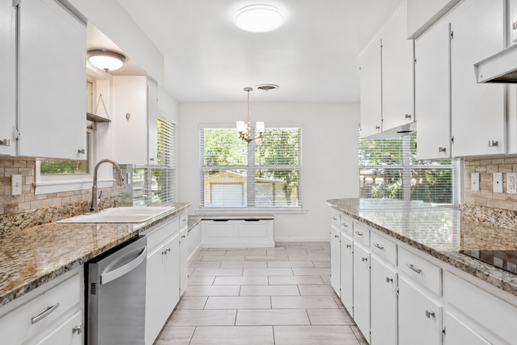 Galley kitchen with granite countertops, white cabinetry and stainless dishwasher