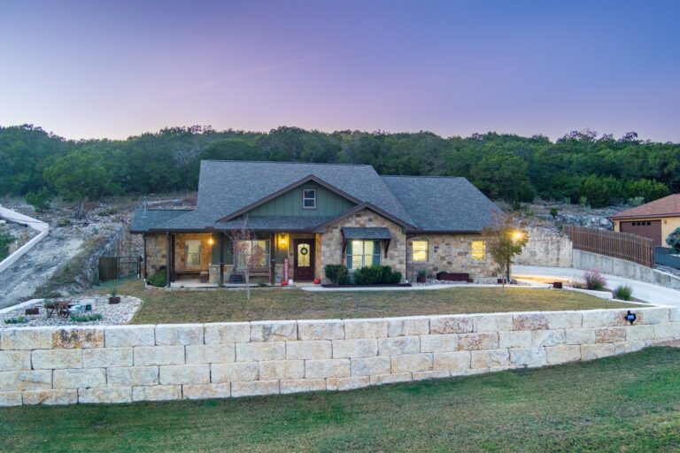 119 Fannin Drive, Kerrville at twilight, windows lit above the limestone retaining wall