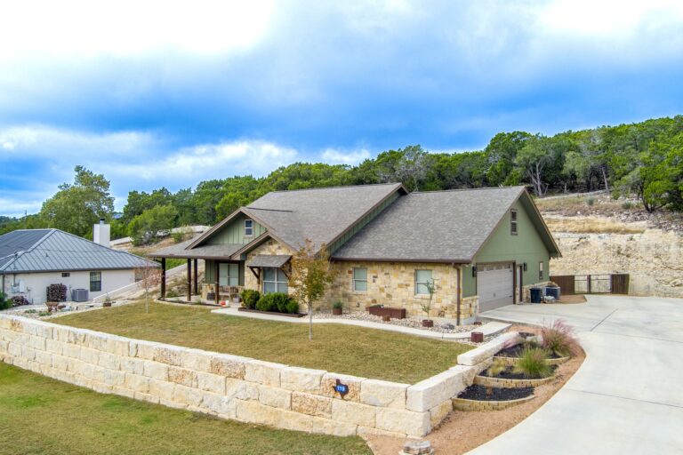 Side view of 119 Fannin Drive, Kerrville showing the two-car garage, wide concrete drive and limestone bluff behind