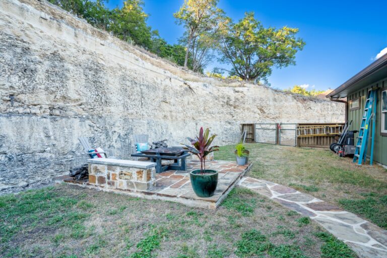 Flagstone patio with a built-in stone bench and fire pit against the cut limestone bluff at 119 Fannin Drive, Kerrville